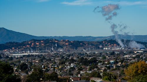 Smoke billowing from a oil refinery with the city of Richmond around it and a mountain in the distance